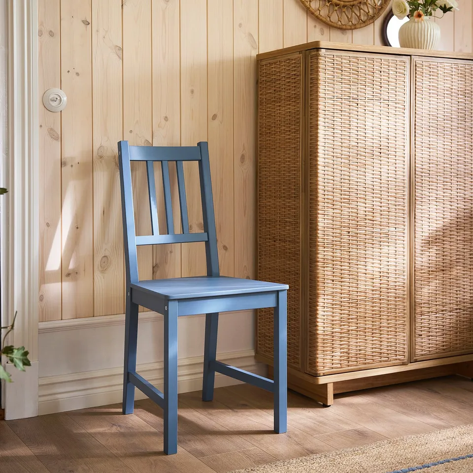 Blue PINNTORP chair against wooden wall, next to wicker cabinet, showcasing compact design.