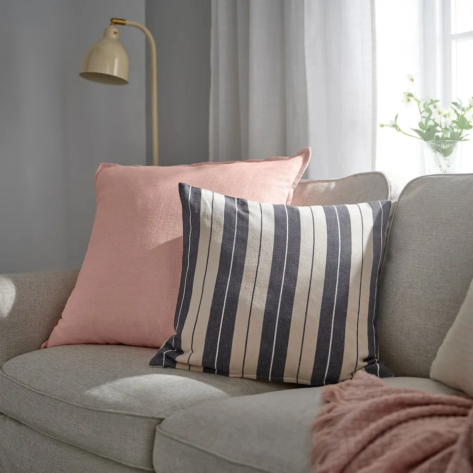 A pink LAGERPOPPEL cushion cover on a couch, made from recycled polyester.