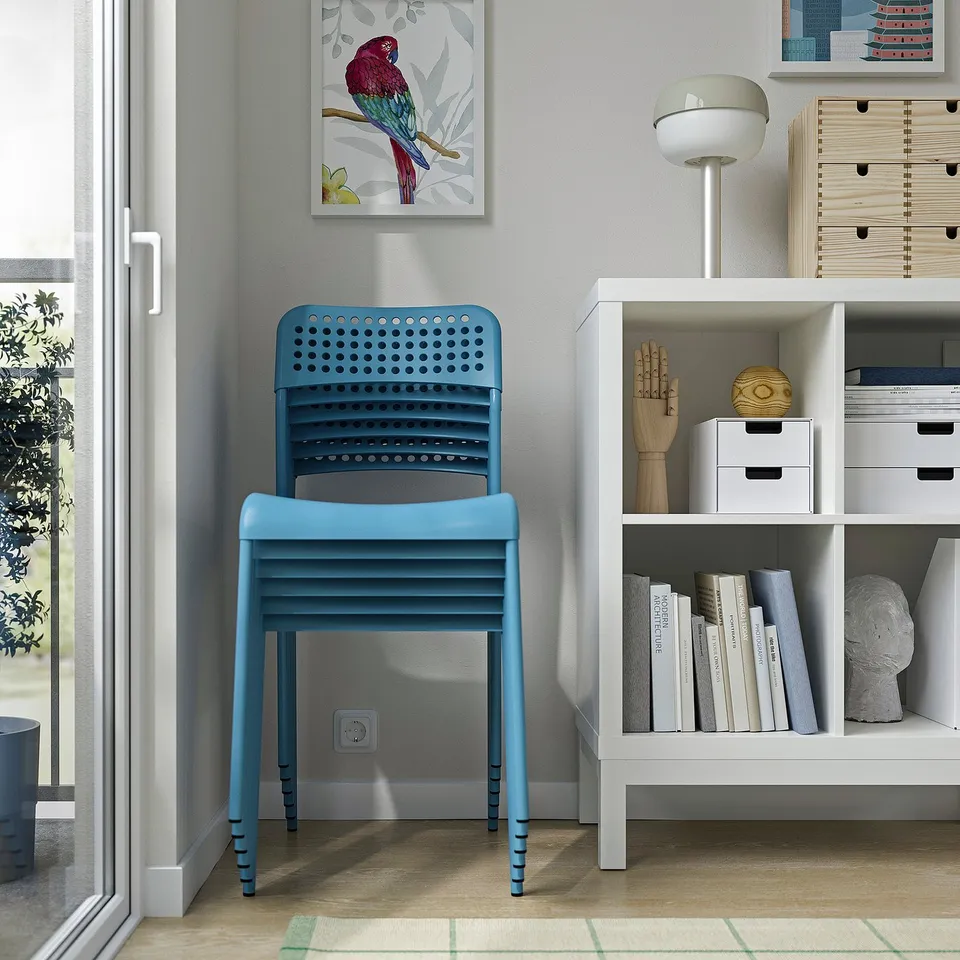 A bright blue stackable chair sits next to a white bookshelf filled with books and decorative items.