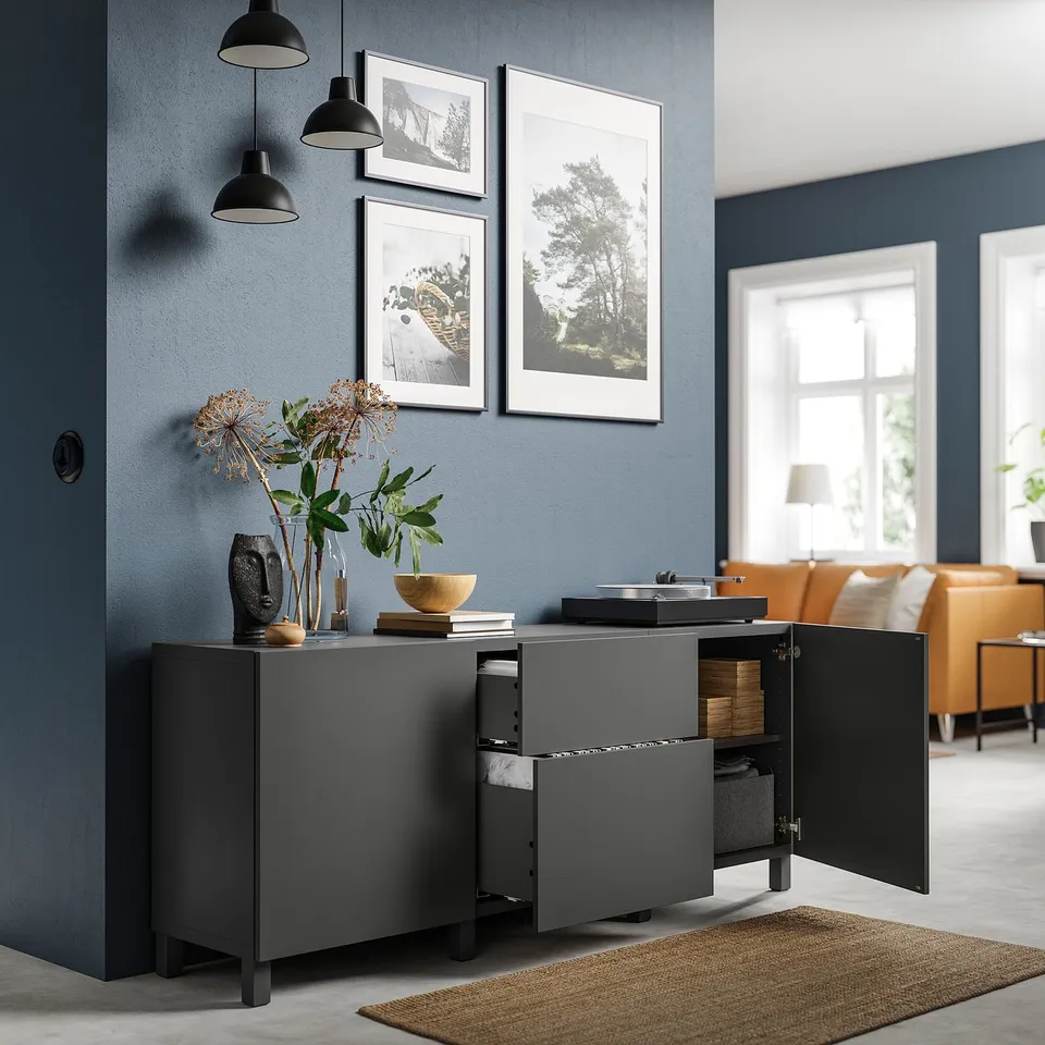 Modern grey BESTÅ sideboard with adjustable shelves and drawers, lit by black pendant lamps. Framed photos and dried flowers decorate the top.