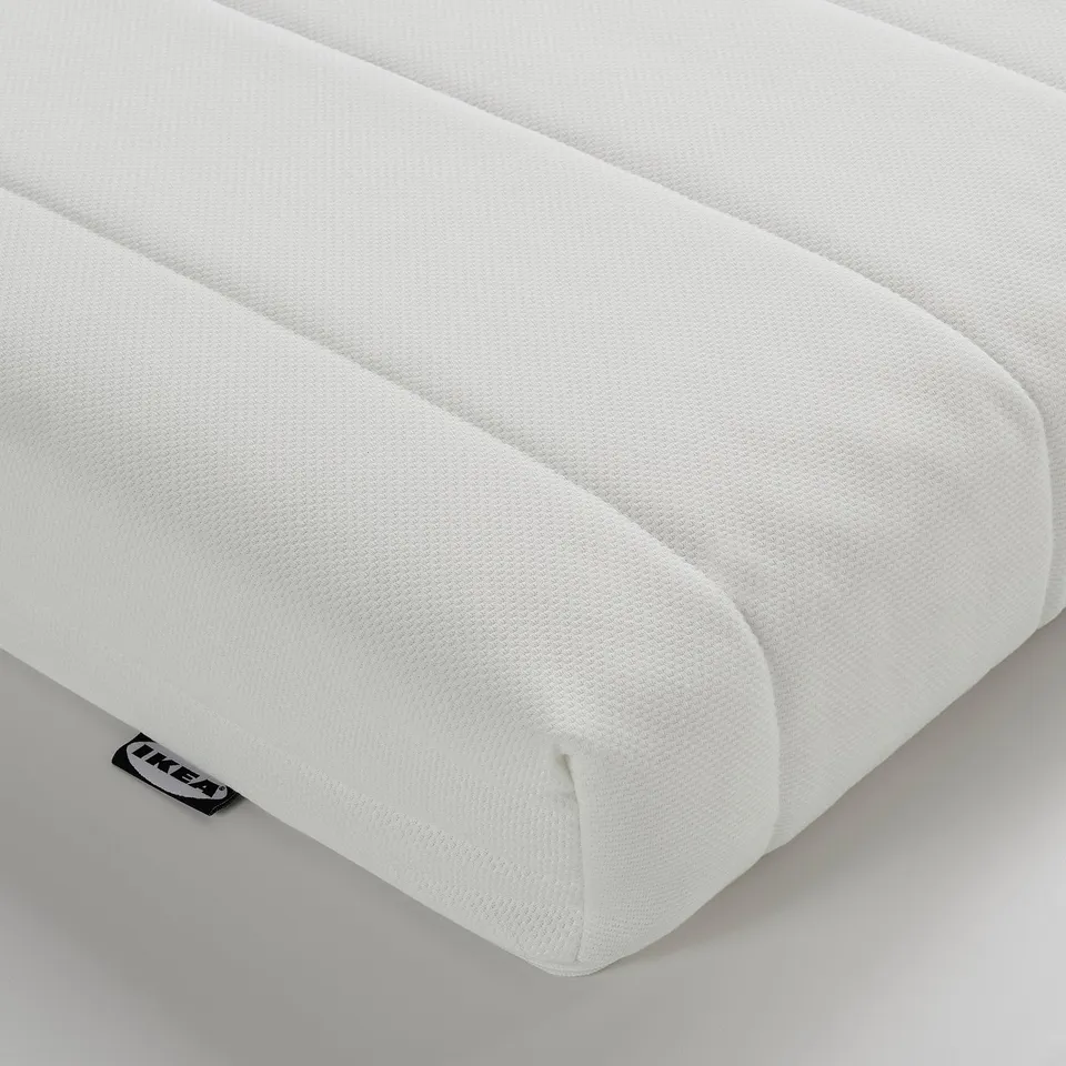 Close-up of a white, textured foam mattress corner, branded IKEA.