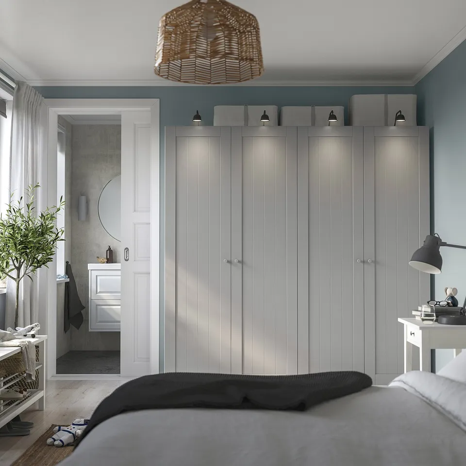 Minimalist bedroom with grey GULLABERG wardrobe, large mirror, and sleek accessories. Wardrobe towers over bed, providing ample storage.
