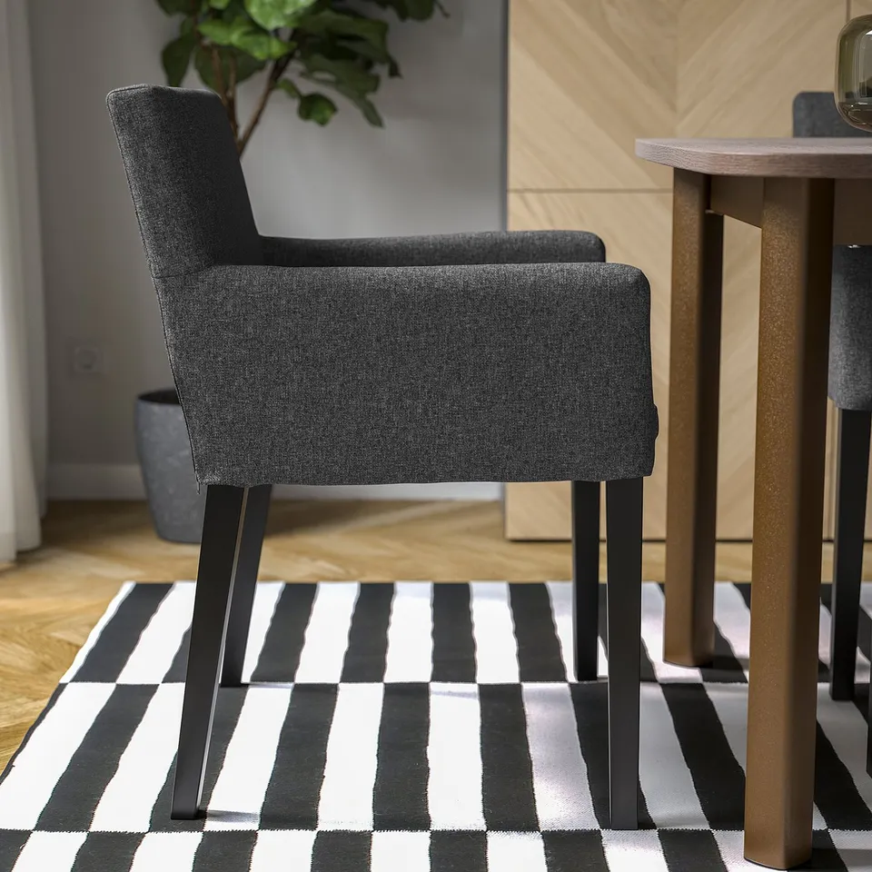 A modern dining chair with dark grey upholstered seat and back, black metal legs on a striped rug.