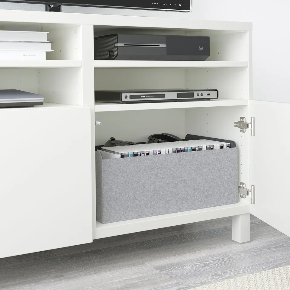 White BESTÅ tv stand with adjustable shelves, showing xbox, media player, and organised gaming accessories behind soft-close doors.