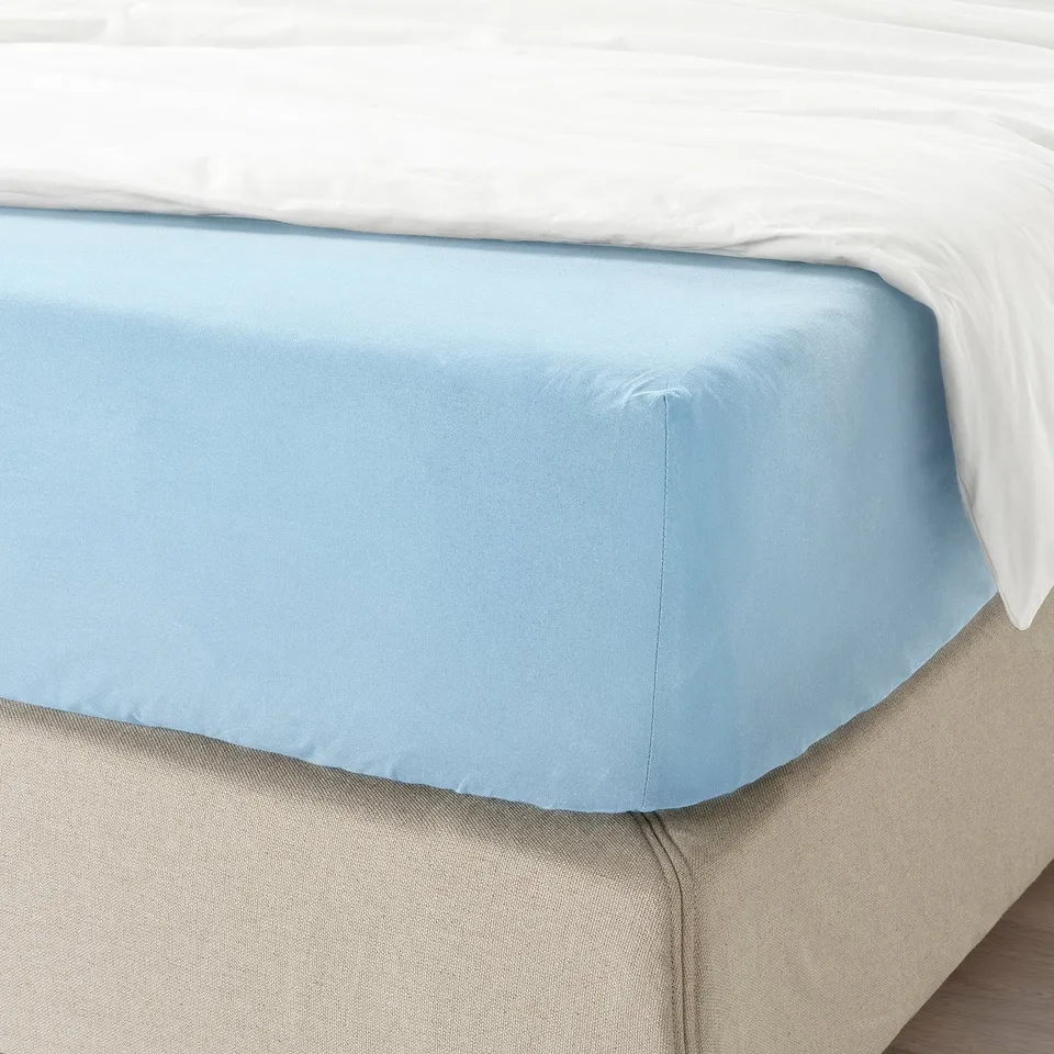 A fitted blue cotton sheet on a bed, showing its soft, breathable texture and secure fit with elastic edges.