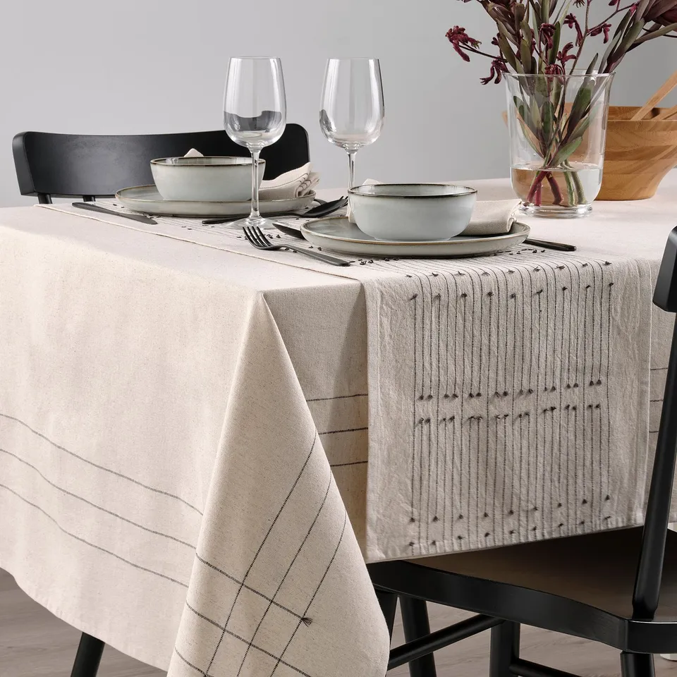 Table set with beige VÅRARV runner, plates, glasses, bowls, and cutlery. Chairs and decorative vase present.