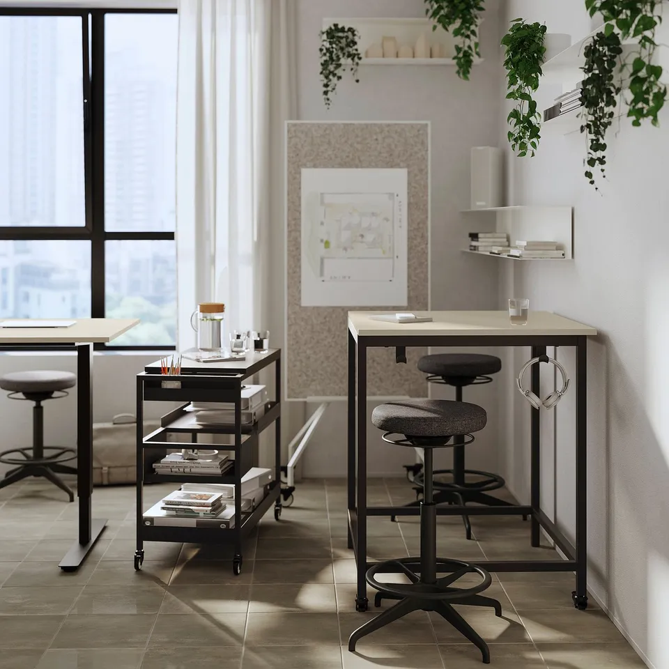 Modern office space with high stools and desks, large windows, plants, and minimalist decor.