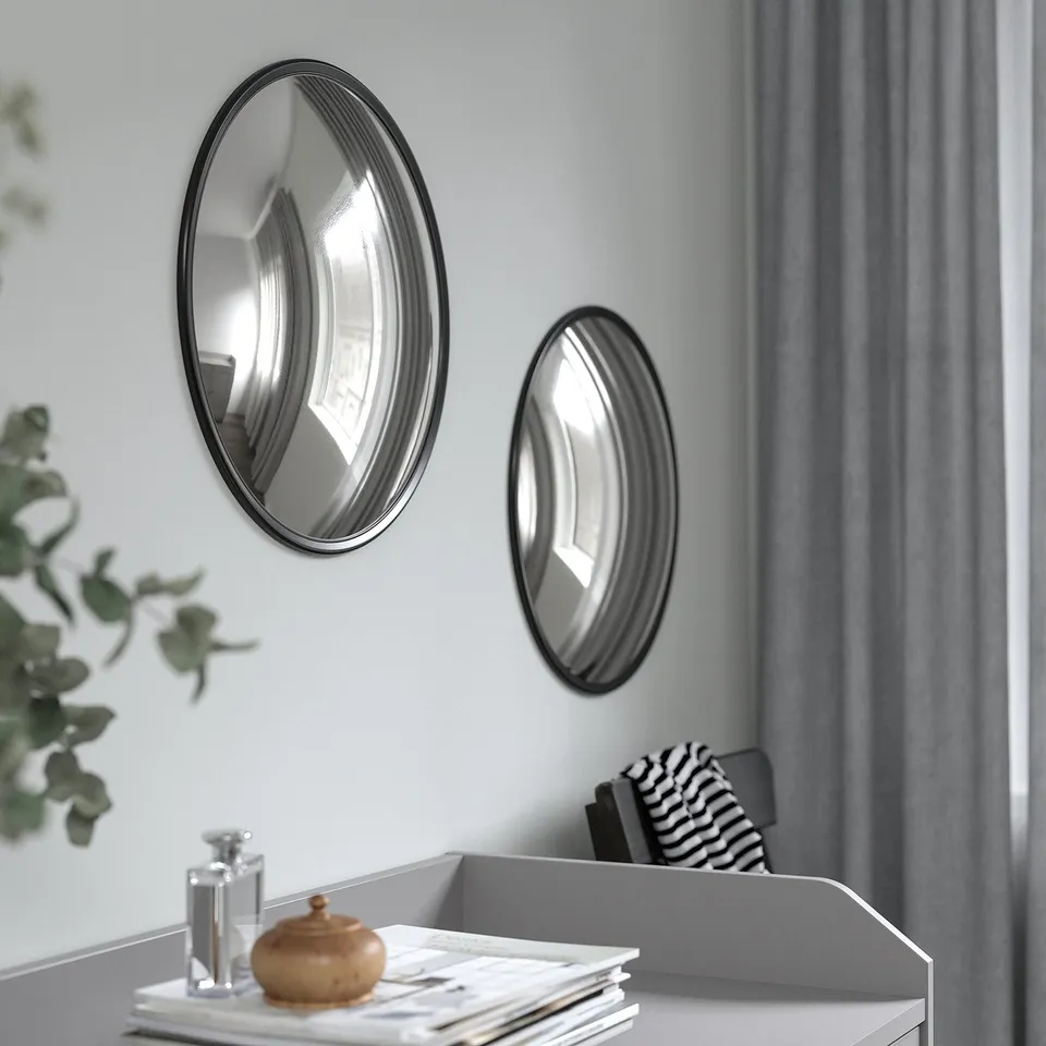 Two round mirrors hang on a wall, reflecting light and adding depth. A white desk sits below with a stack of books, a vase, and a wooden box.