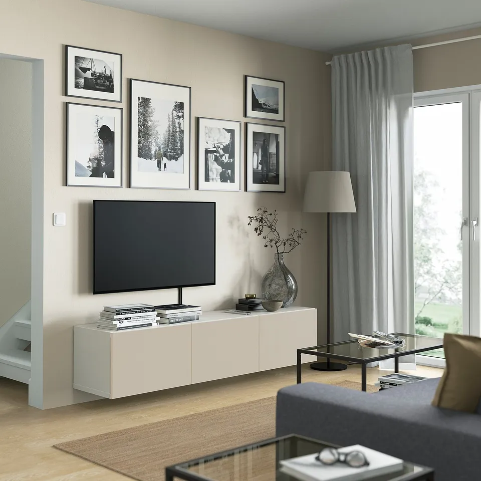 Modern living room with BESTÅ tv bench, large tv, grey sofa, and lamp. White with black & white photos, grey curtains, light wood floor.
