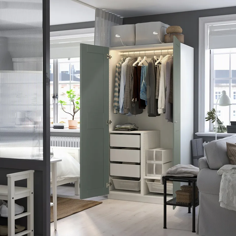 Modern, green, open wardrobe displays clothes, drawers, and organiser. Integrated lighting highlights hanging garments and storage.