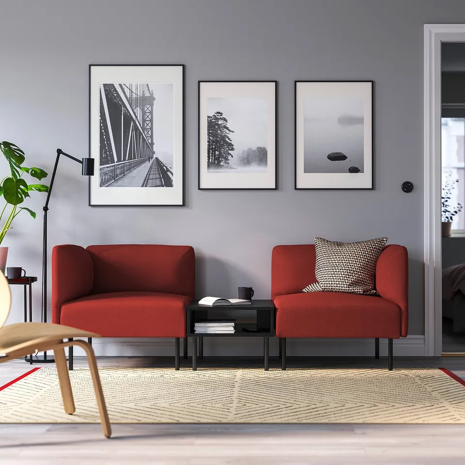 Modern living room with red LILLEHEM sofa, black table, patterned rug, and three black-and-white artworks on a light grey wall.