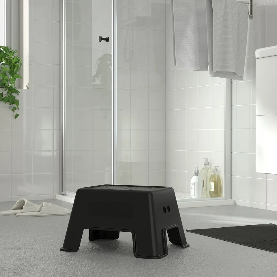 Black BOLMEN stool in modern bathroom, small & sturdy, fits near white tiles & glass shower.
