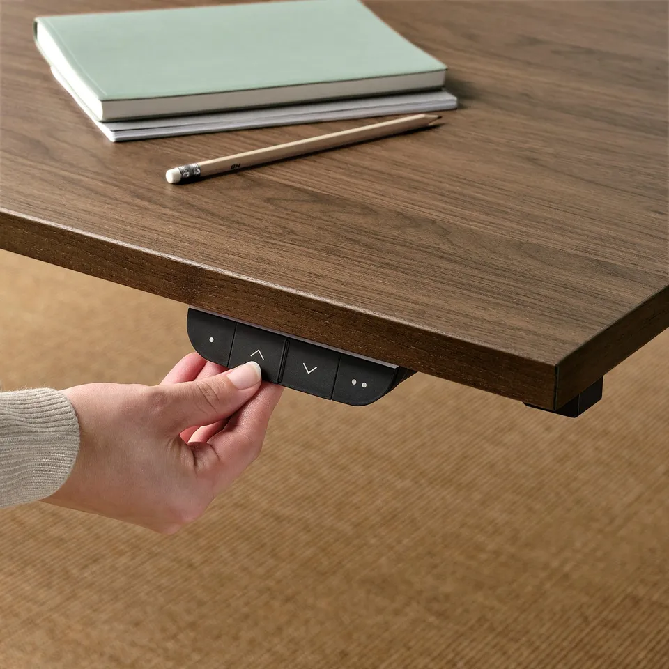 Person adjusting height of sit/stand desk using control panel. Desk has memory settings for comfort.