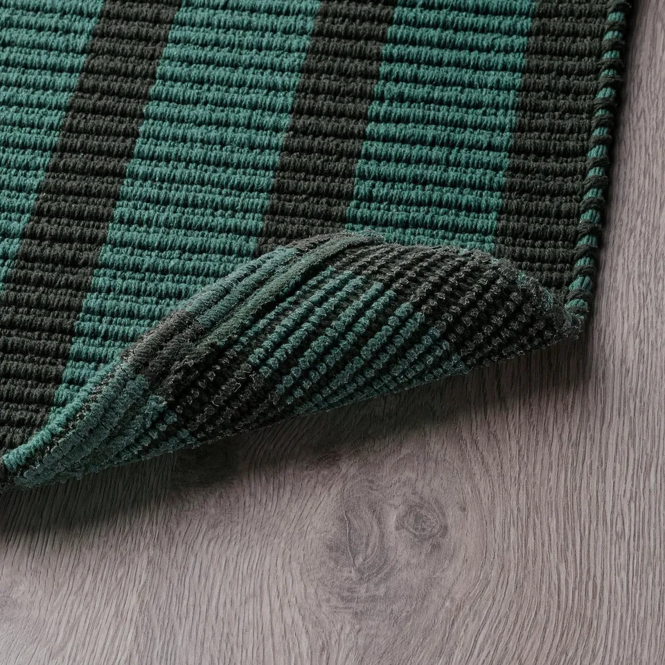 Green and black striped door mat with anti-slip backing on wooden floor.