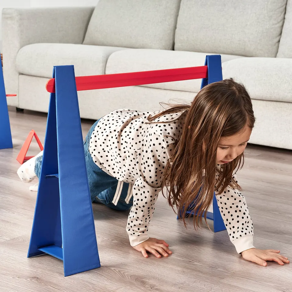 Child crawling under red-blue obstacle course hurdle.