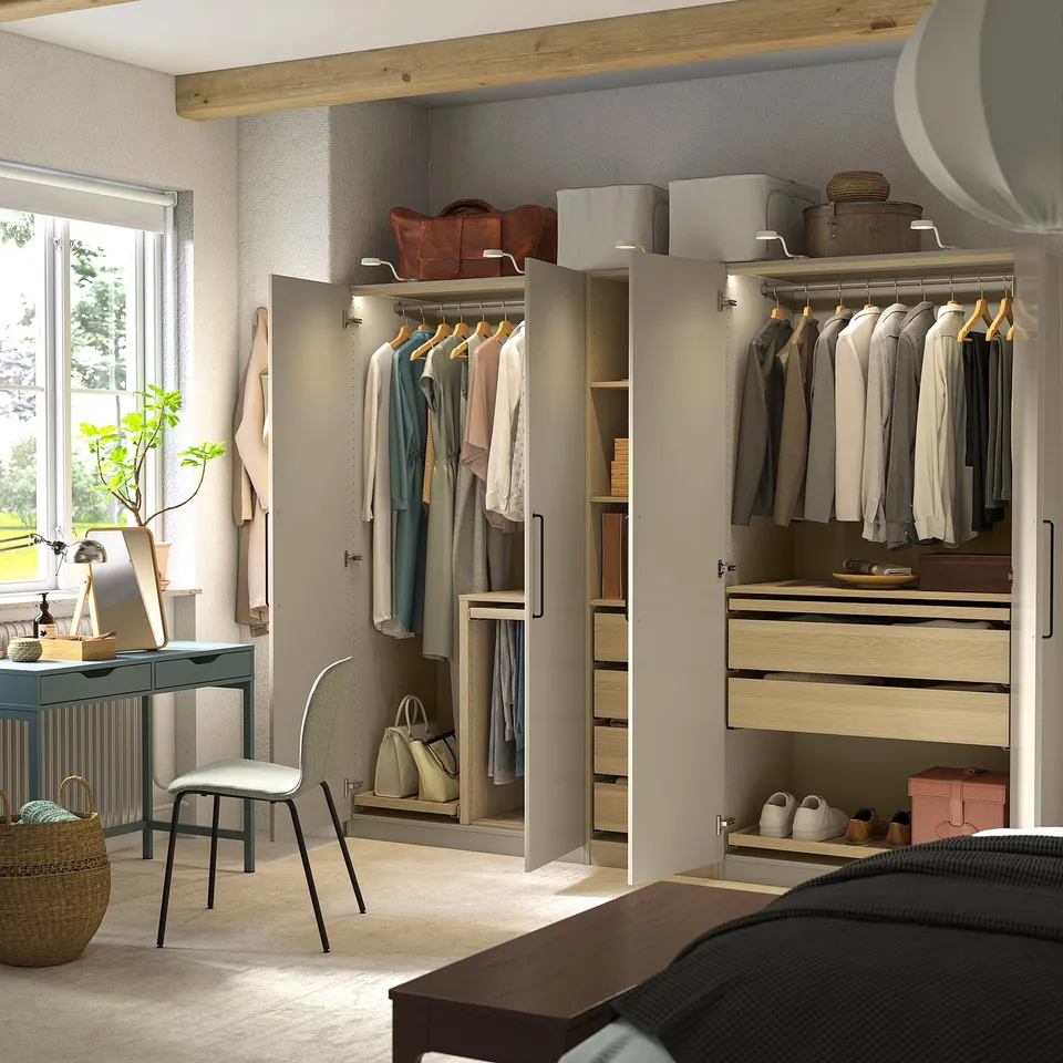 A modern bedroom with open PAX wardrobe, desk, chair, and plant.