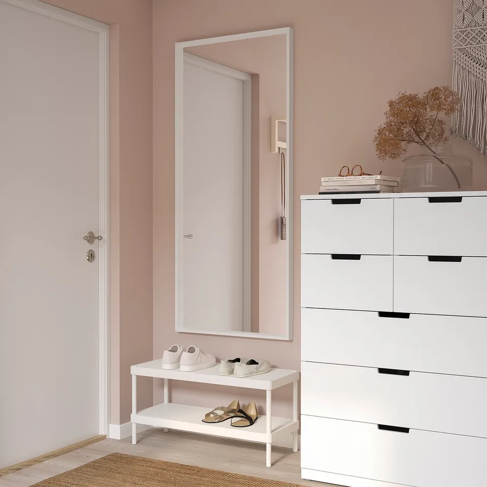 Stylish entryway with large white NISSEDAL mirror, sleek shoe rack, and white drawers. Pinkish walls, modern decor.