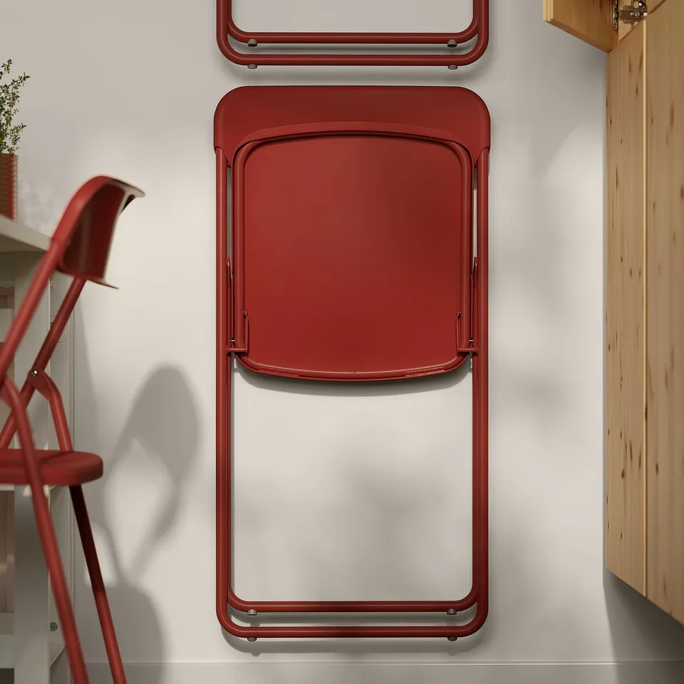 Red foldable chairs and table stack against wall. Easy to store, sturdy metal frames.