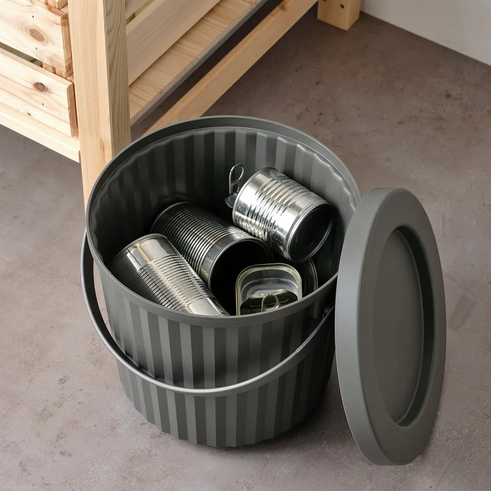 A striped bin holds metal cans, with a lid nearby. Used for sorting small waste.