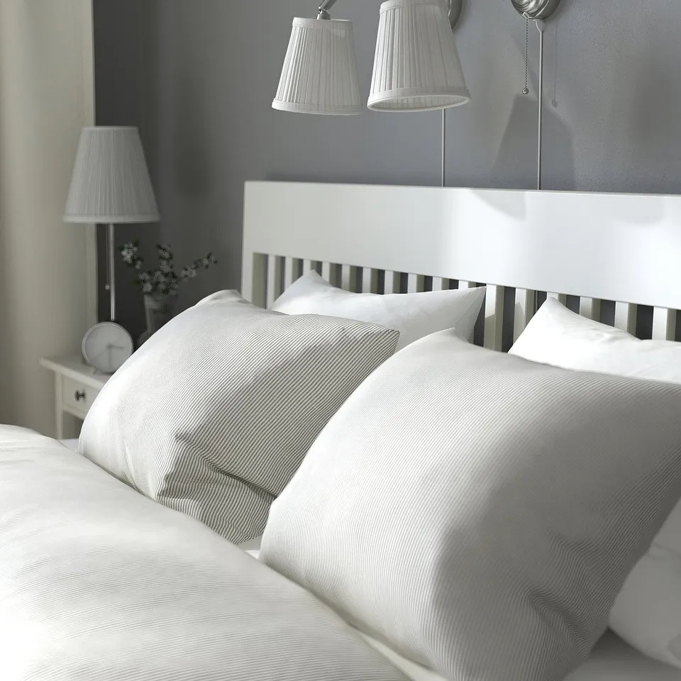 Cosy bed with white lamps, two pillows, and a clock on bedside table.