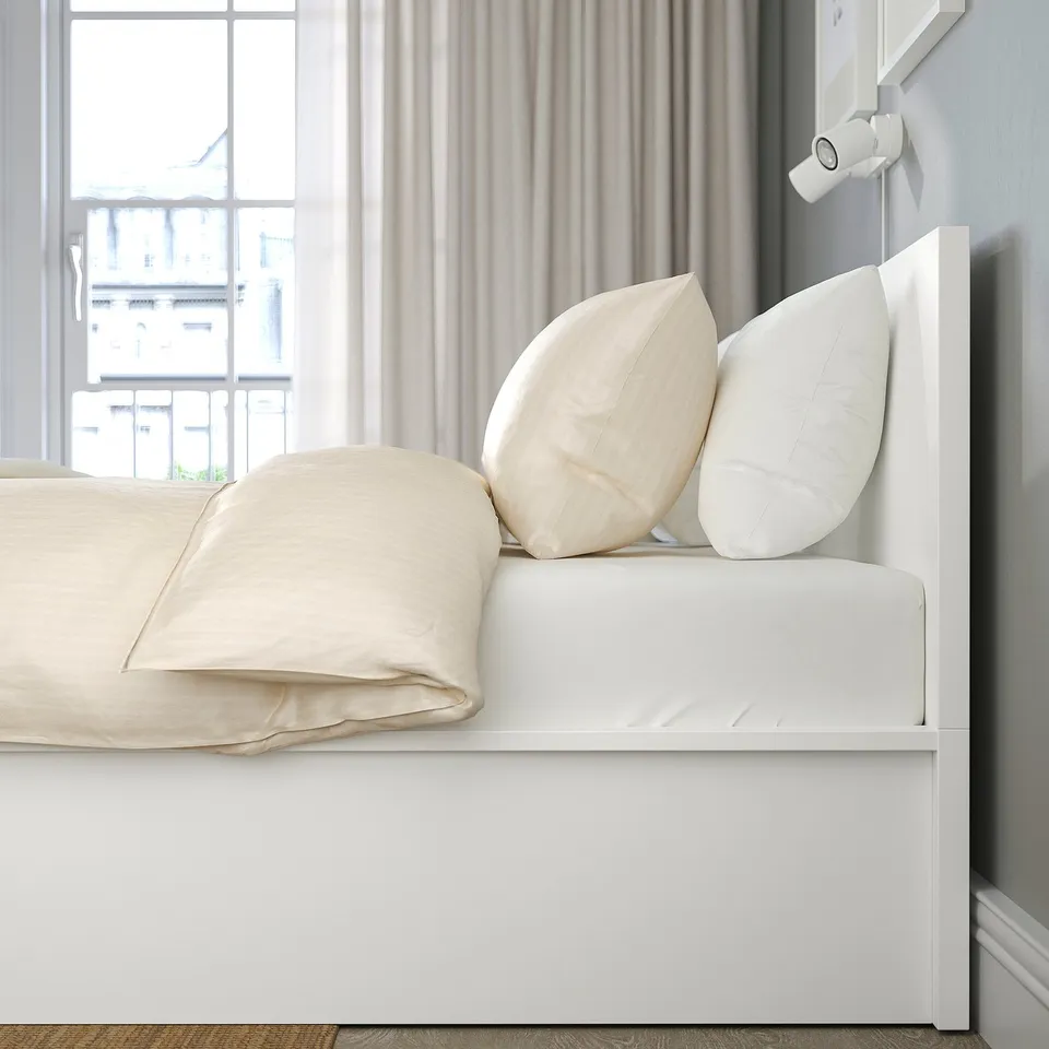 Bed with lift-up base for storage, visible via headboard and partially lifted base revealing white linens and pillows.