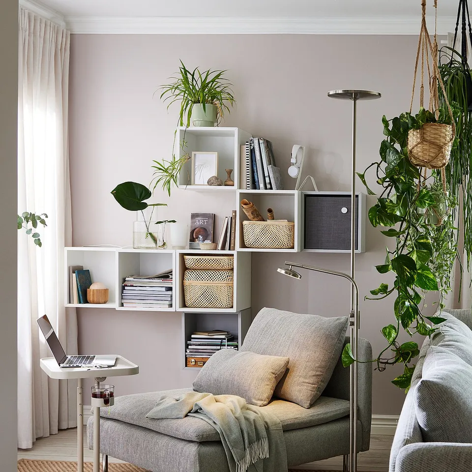 Cosy living room setup with grey SÖDERHAMN sofa, stylish shelves, hanging plants, and a laptop table.