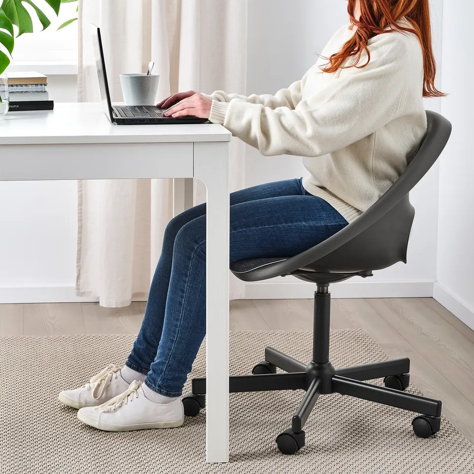 Person sitting on black office chair with height adjustment, using laptop on white desk.