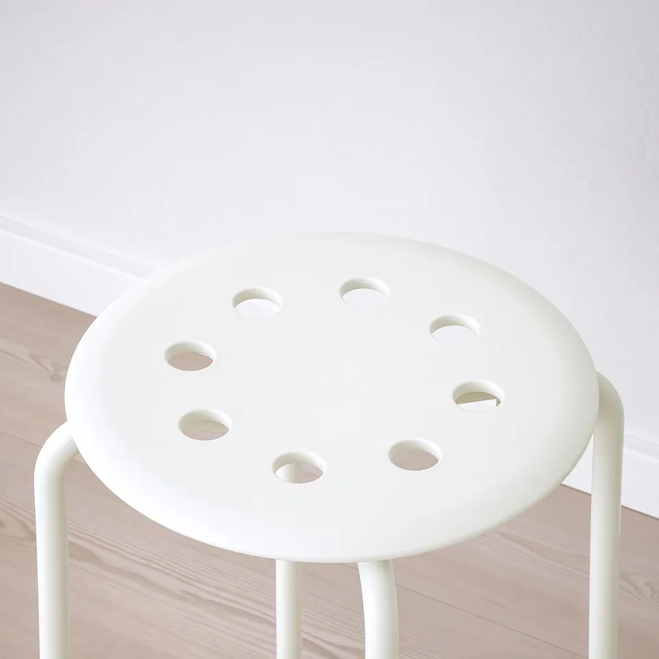 A sleek white stool with four round cut-outs, resting on a wooden floor. Minimalist design, sturdy build quality.