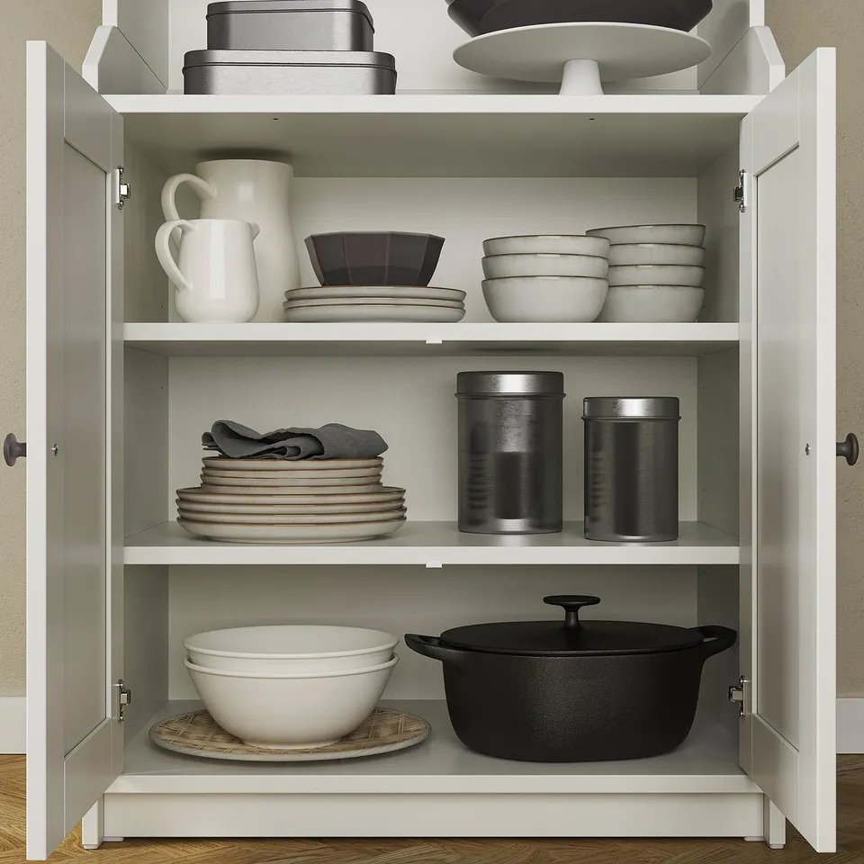 Open white cabinet with plates, bowls, pitchers, towels, and pots neatly arranged on three shelves.