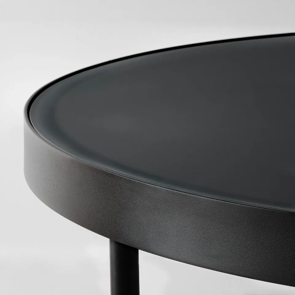 Modern round black side table with sleek glass top; sturdy steel legs, refined finish.