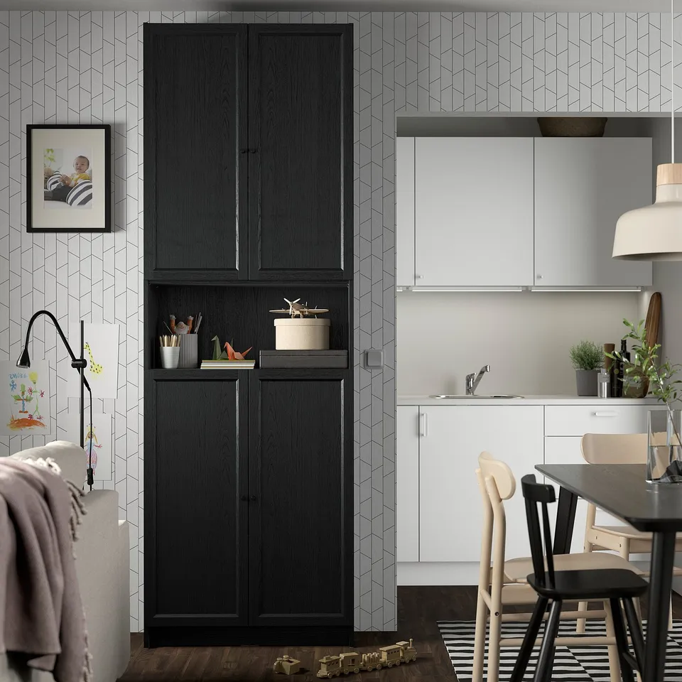 Modern living room with black BILLY bookcase, toy train, and white kitchen area.