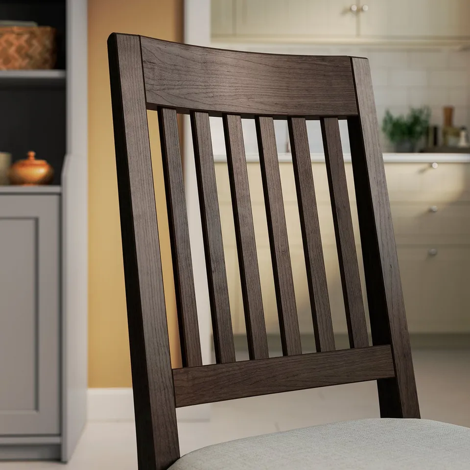 Dark wood chair with vertical slats, cushioned seat in light fabric, placed near kitchen cabinets.
