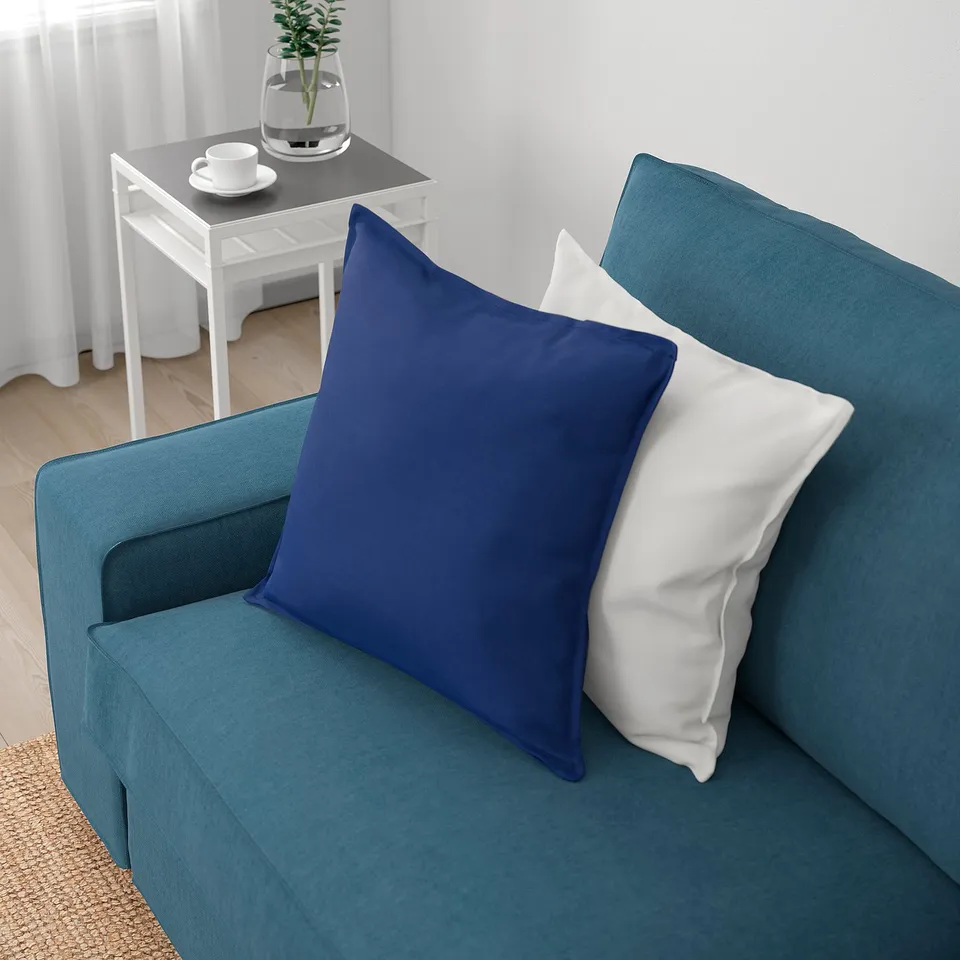 Blue KIVIK sofa with deep cushions and white pillows, ideal for relaxing. Plant and cups on white side table beside it.