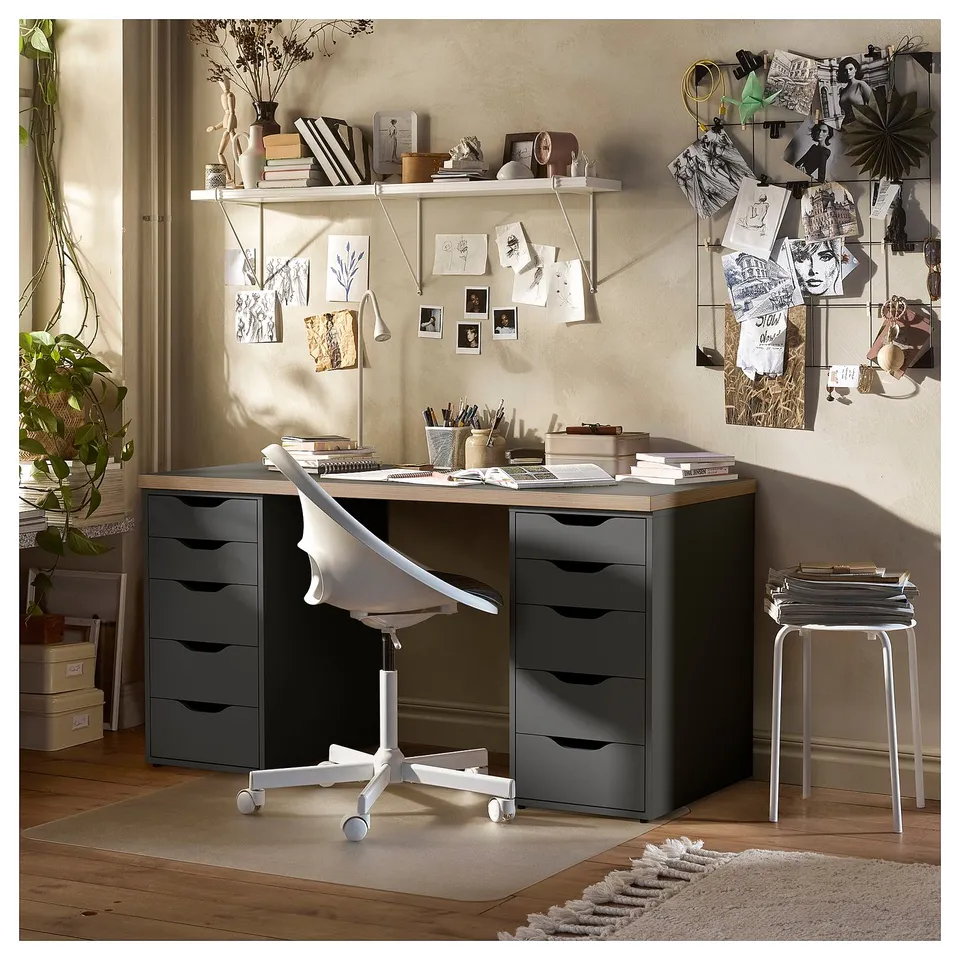 Home office setup with lagkaptan desk, grey drawers, wooden top, plants, posters, and chair.