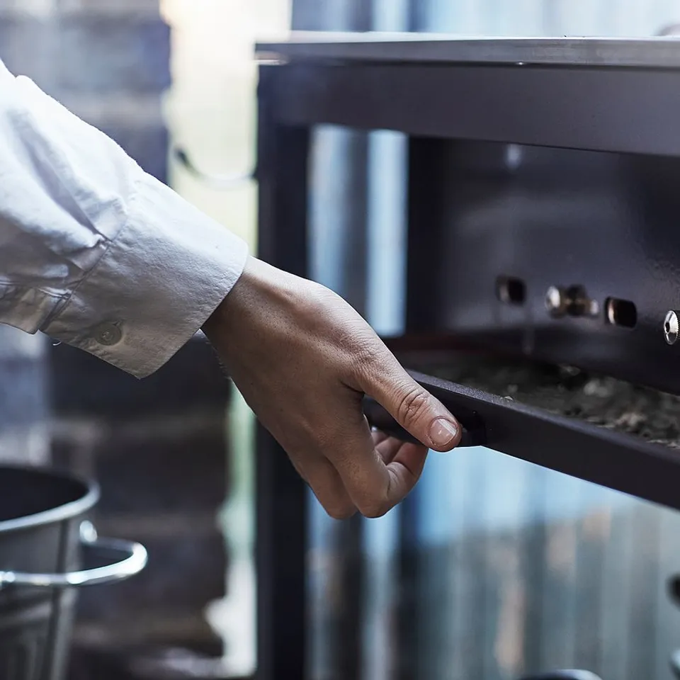 A hand adjusts a black stainless steel grill handle.