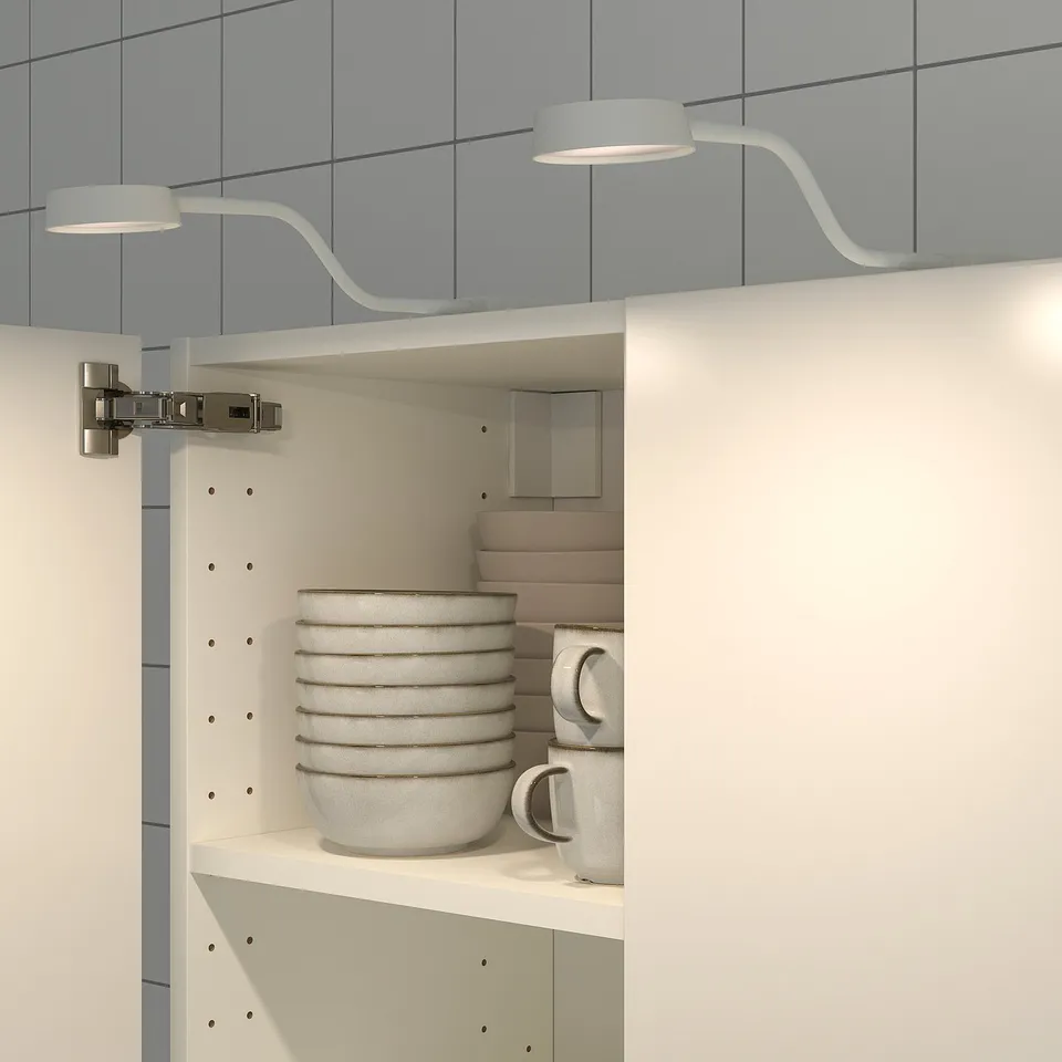 Cabinets lit by bendable, slim lamps with gooseneck arms directing soft light onto stacked bowls and mugs.