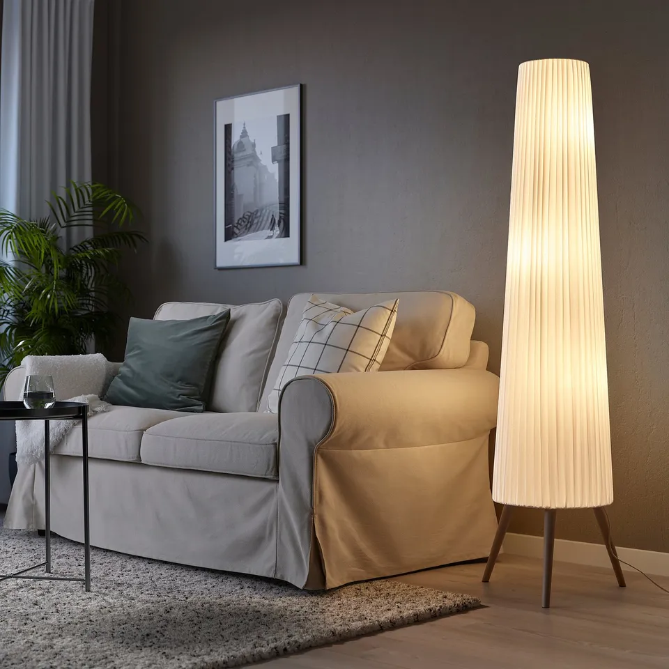 Modern living room with grey floor lamp, sofa, coffee table, plant, rug, dark wall art.