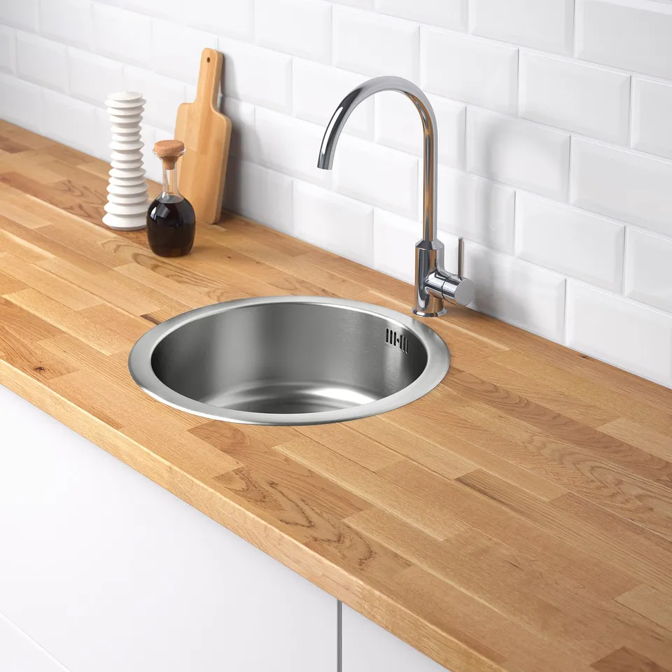 Modern kitchen sink with polished stainless steel basin on wooden counter. Includes curved tap and sound-absorbing material.