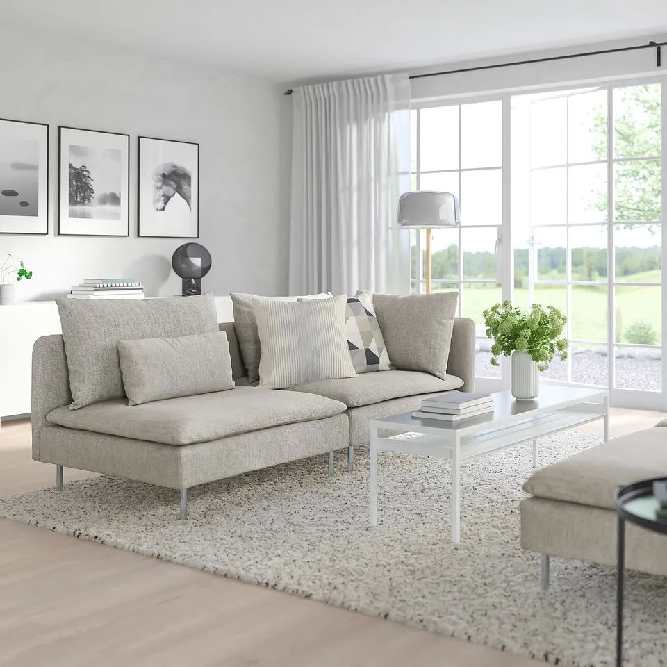 Modern minimalist living room with large grey SÖDERHAMN sofa, low coffee table, and large windows showing green outdoors.