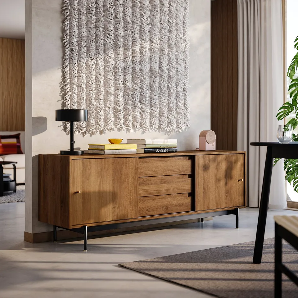 Wooden tv bench with sliding doors, drawers, and metal legs against wall with art. Black lamp and decor on top. Fits spacious room with black chair.
