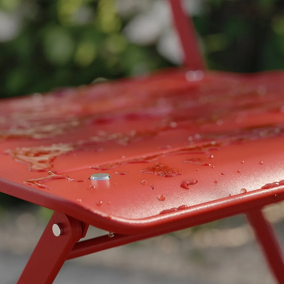 Red metal outdoor table with water droplets, part of the SUNDSÖ collection.