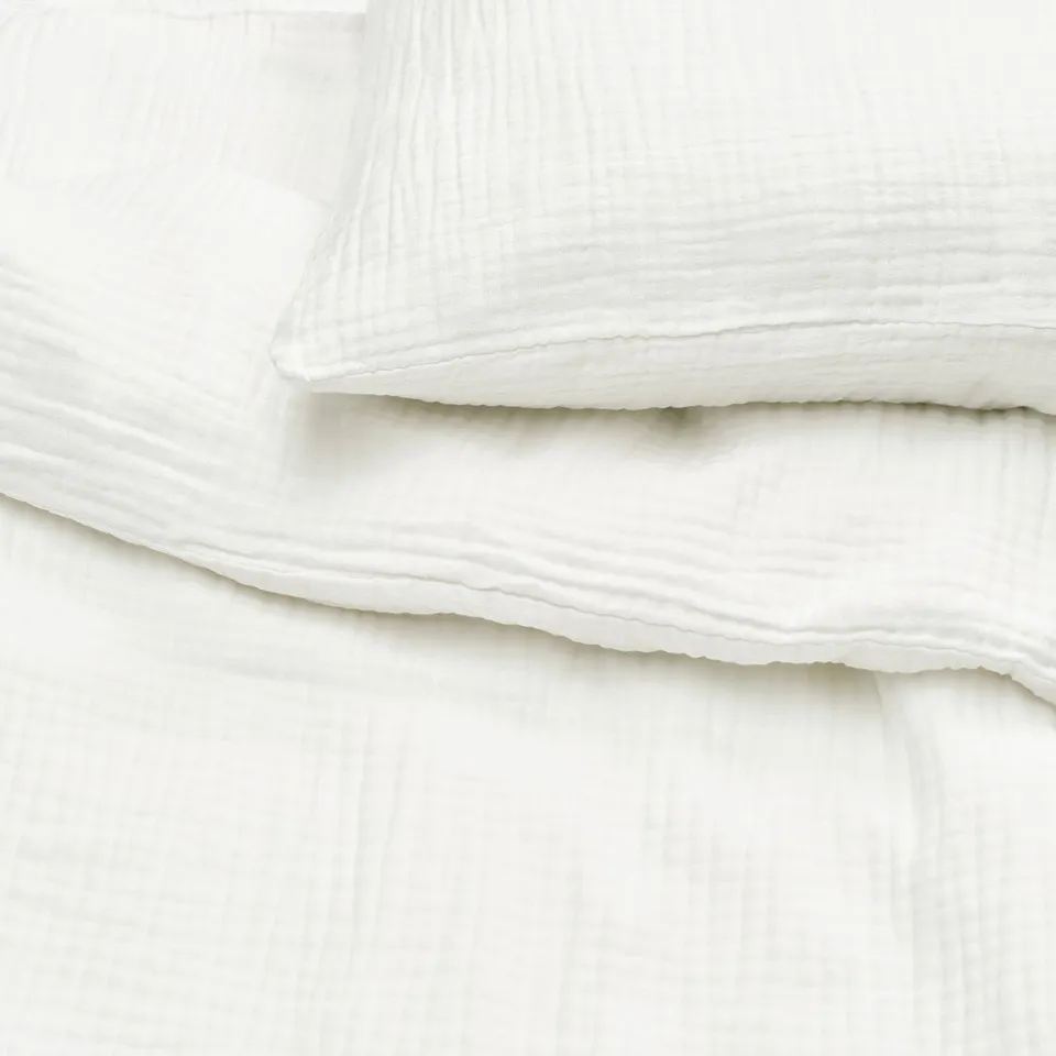 Clean, crisp white bedding set, featuring smooth cotton texture. Duvet and pillowcases have subtle, sophisticated details.