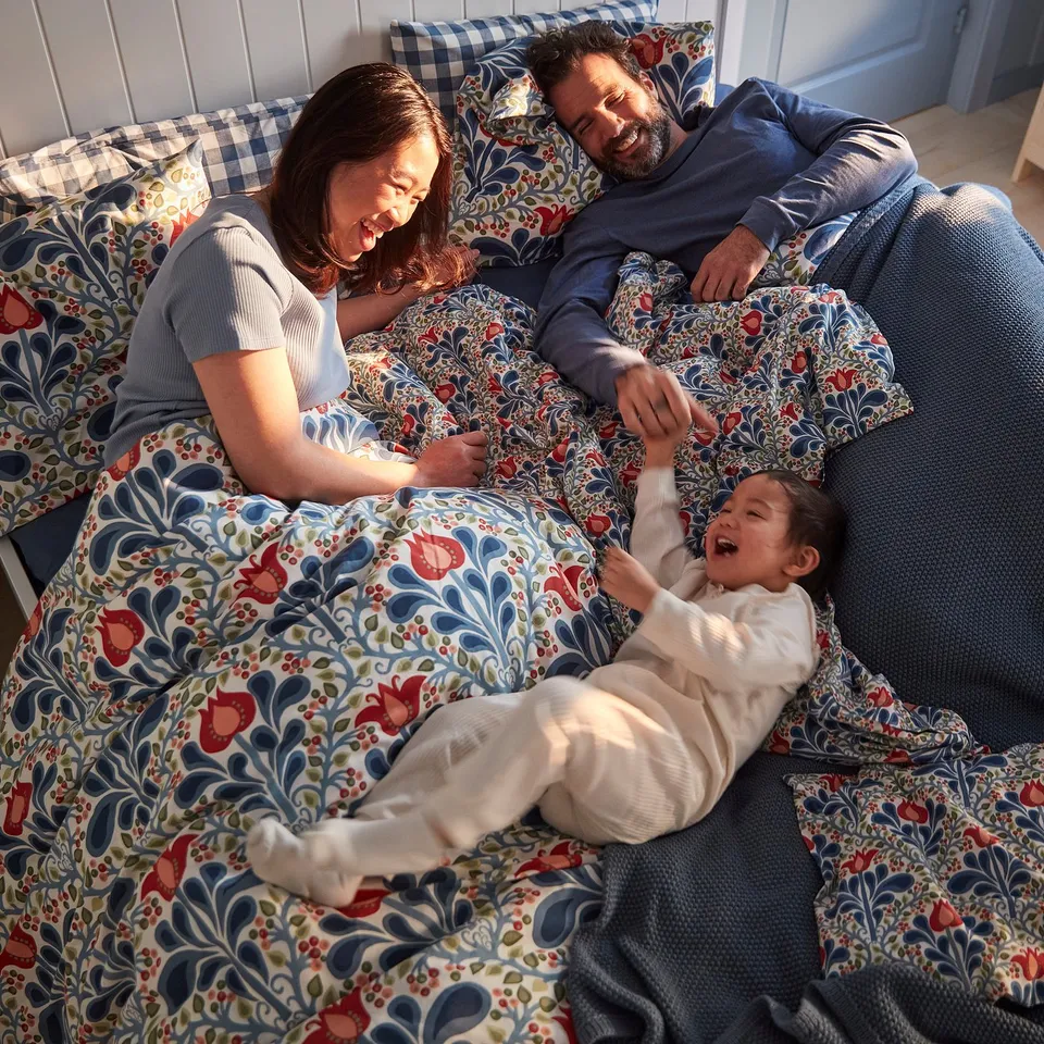 Family enjoying SÄTERVIDE duvet on a cosy, floral-patterned bed.