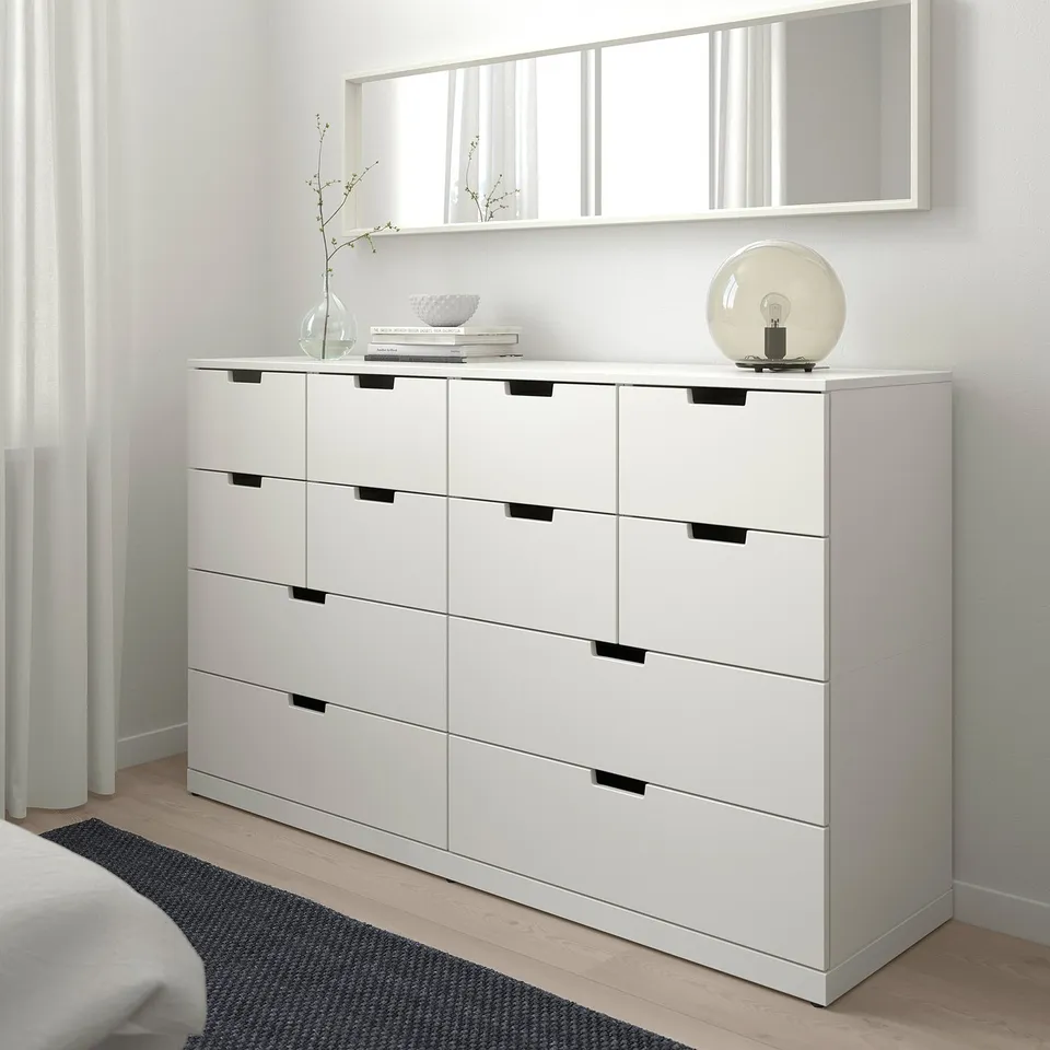 White NORDLI chest with 6 black-handled drawers in bright bedroom near window.