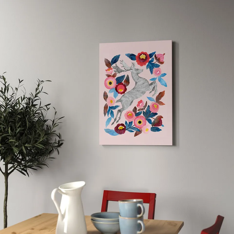 Canvas art with deer and flowers hangs on a wall above a wooden table with cups and a plant.