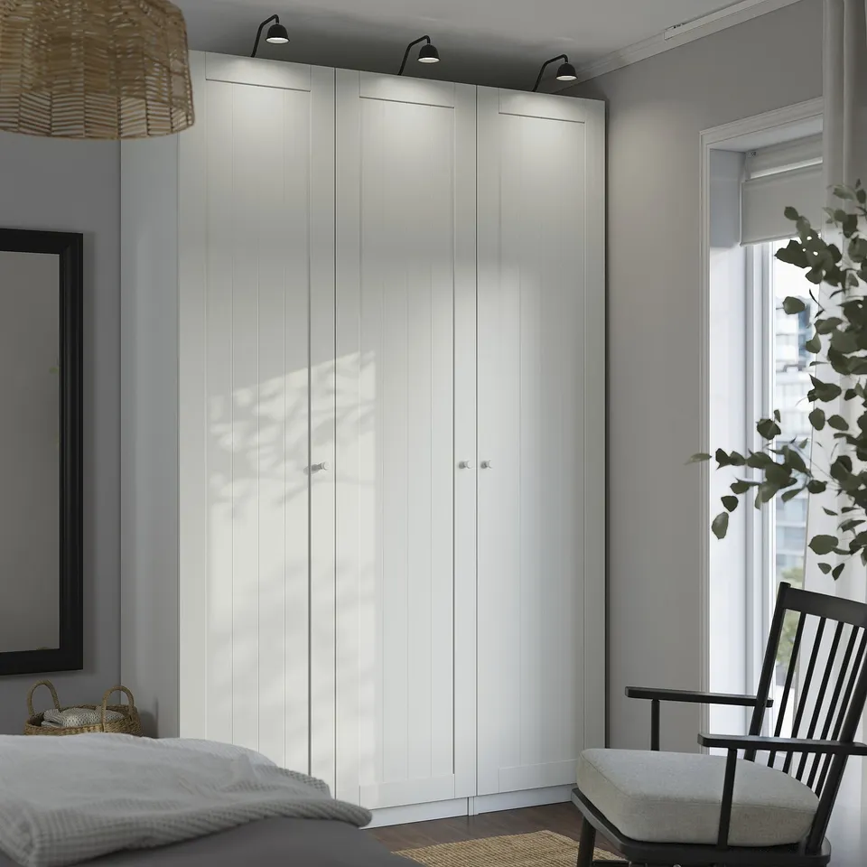 Modern bedroom with large white PAX wardrobe, black framed mirror, and hanging chair near window.