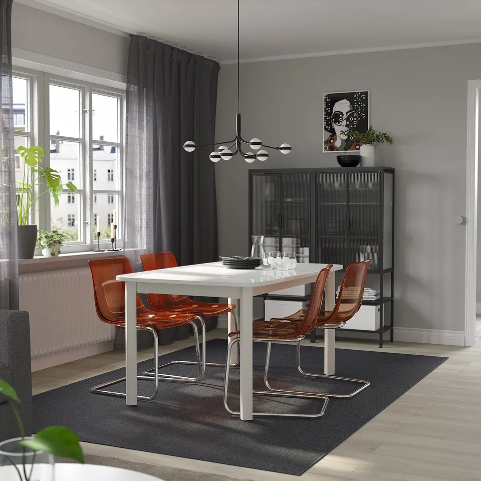 White extendable dining table in modern dining room with orange chairs, large windows, and artwork.