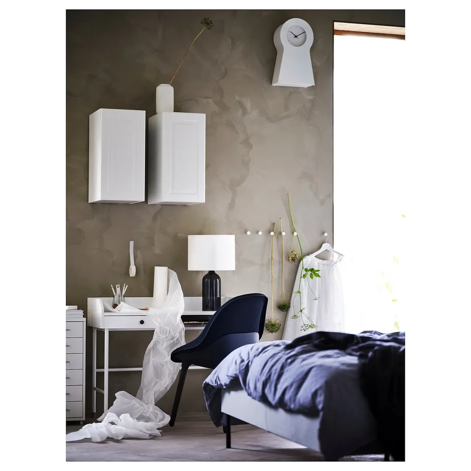 Modern bedroom with monochromatic decor, featuring a desk, floating cabinets, bed, and clock.