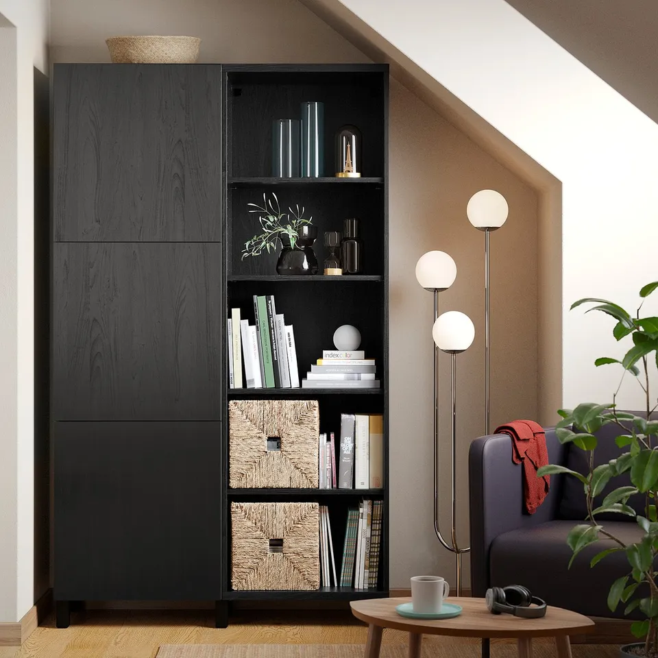 Black BESTÅ unit with books, plants, decor, grey chair, table, lamps.