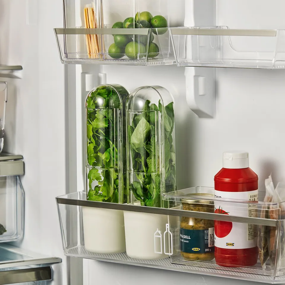 Fridge organiser with clear containers holding greens, limes, and condiments. Dome-shaped storage keeps herbs fresh.